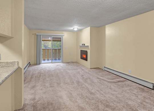 An open living room space here at Hillside Chalet with a carpeted floor and a sliding door window with a view of trees. A cozy fireplace sits against the wall next to the sliding doors.