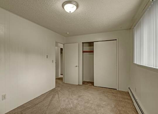 A spacious, empty bedroom here at Montclair with beige carpet, light paneled walls, and a sliding-door closet for convenient storage.