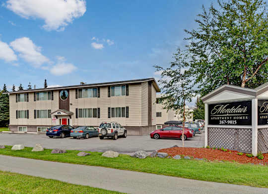 A welcoming exterior view of Montclair with a three-story apartment building, onsite parking, and a landscaped sign reading “Montclair Apartment Homes.”