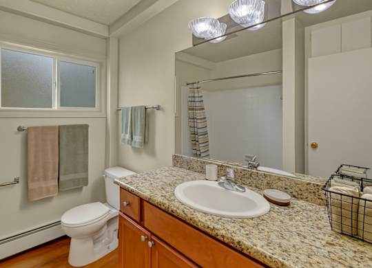 A clean bathroom here at Montclair with a wood vanity, speckled granite-style countertop, and a large mirror above a white sink.