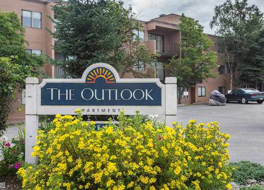 The Outlook apartments are surrounded by greenery and have a sign in front.