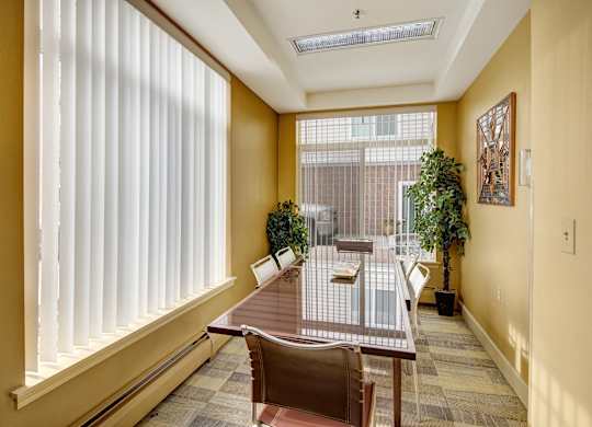 A bright meeting room here at Park Plaza II with a long glass-top conference table and modern chairs, featuring large windows with vertical blinds, warm wall tones, and greenery for a professional, welcoming space.