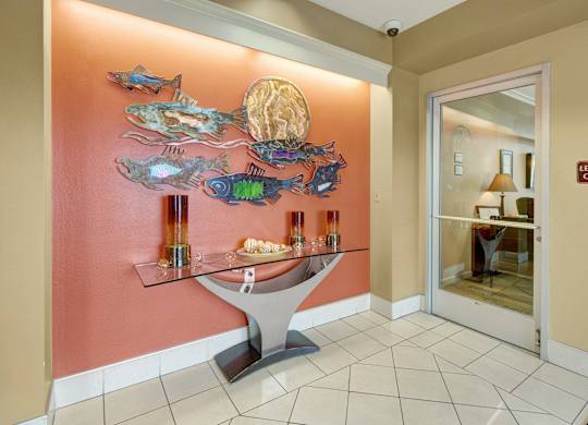 A welcoming lobby entry with tiled flooring and warm accent walls, featuring a glass console table with decorative accents and a convenient doorway leading into the leasing office.