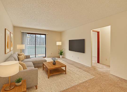 A bright living room here at Park Plaza with a light gray sectional sofa, wooden coffee table, cozy neutral rug, and a sliding glass door opening to a balcony with soft natural light, creating a cozy and welcoming space.