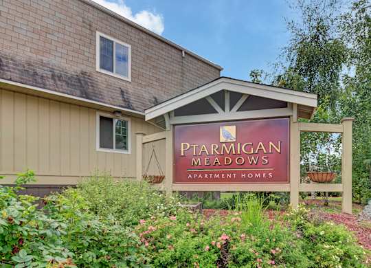A sign for Ptarmigan Meadows Apartment Homes is displayed in front of a building.