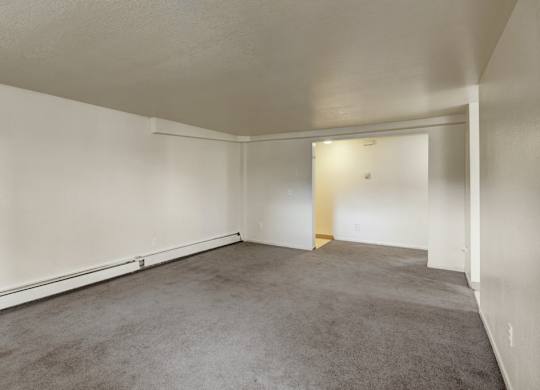 A spacious, empty living room here at Ptarmigan Meadows with soft gray carpet, clean white walls, and an open layout that offers plenty of room for flexible furniture placement.