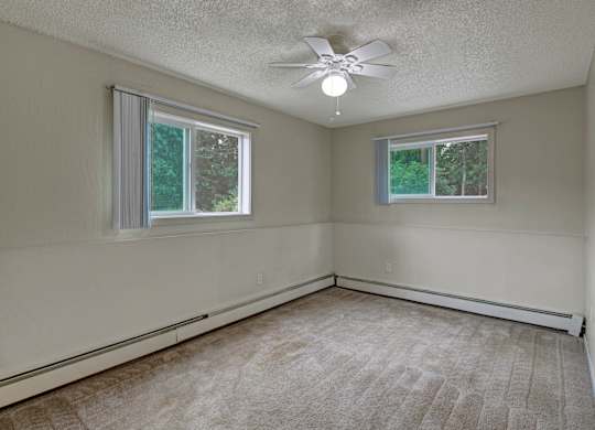 A room with a ceiling fan and two windows.
