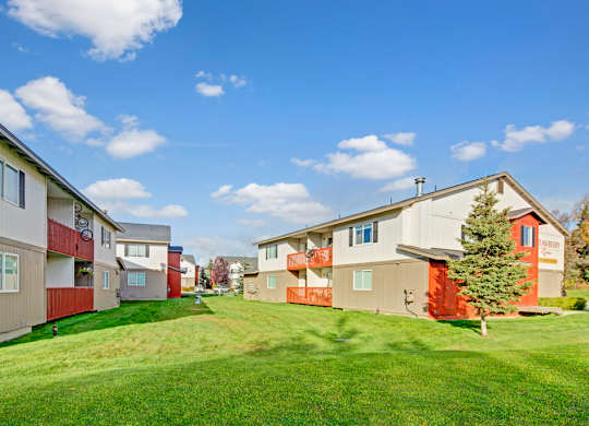 A sunny community courtyard here at Strawberry Lane with wide green lawn space, red balcony railings, and well-kept apartment buildings that create an open, neighborhood feel.