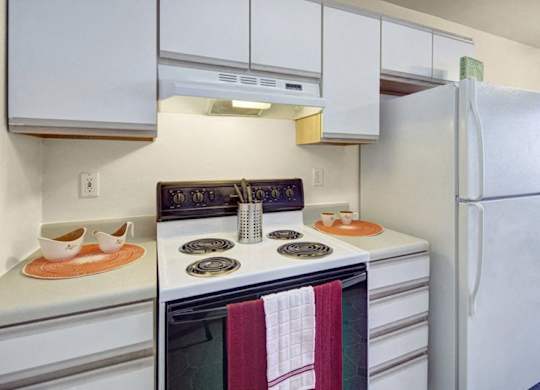 A clean kitchen here at Timber Ridge with white cabinets, white countertops, and a white refrigerator, featuring an stove with range hood and a simple, bright layout for everyday cooking.