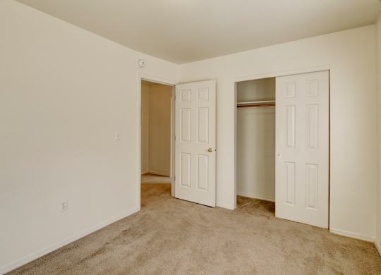 A clean, empty bedroom here at Timber Ridge with soft beige carpet, neutral walls, and a spacious closet with sliding doors, creating a bright and comfortable space for relaxing.