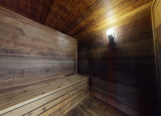 Wood-paneled sauna interior here at The Club at Eagle Pointe Apartments with soft amber lighting, highlighting a warm, rustic bench along the left wall. Cozy, inviting atmosphere.