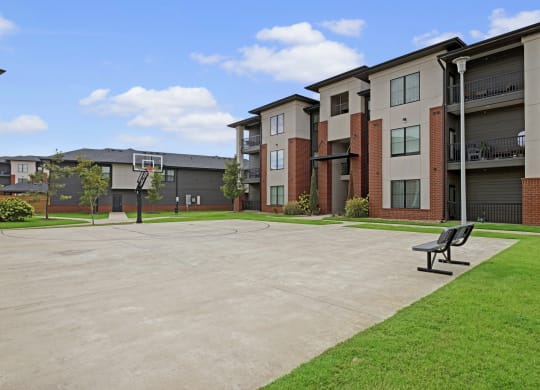 49 Wests's modern apartment complex with brick and neutral tones surrounds a wide concrete basketball court. Benches and lush green lawns add a welcoming feel.