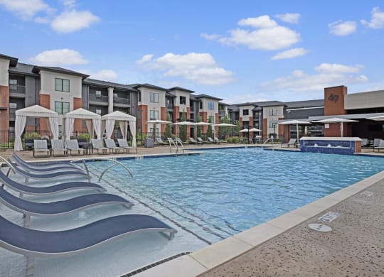Modern 49 West Apartment complex with large outdoor pool and sun loungers. White cabanas line the poolside. Clear blue sky suggests a calm, sunny day.