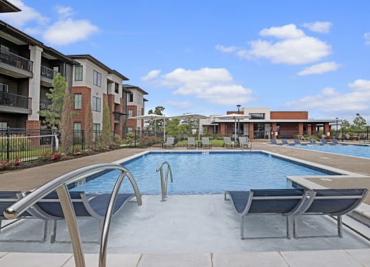 Modern 49 West Apartment complex with a large outdoor pool, poolside loungers, and a clubhouse. Bright, sunny weather with a clear blue sky.