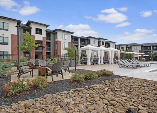 Modern 49 West Apartment complex with a poolside area includes lounge chairs, white cabanas, and a fire pit surrounded by chairs, evoking relaxation under a blue sky.