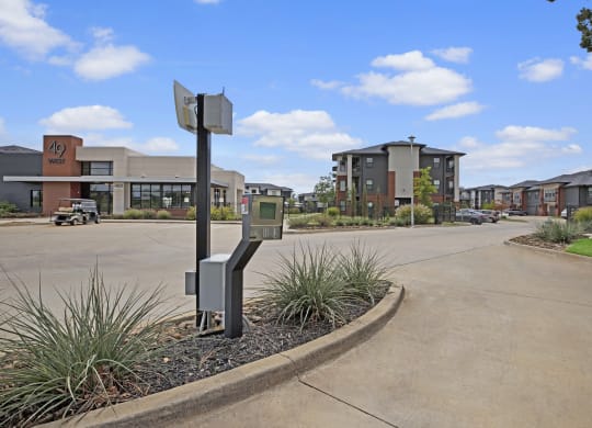 A modern 49 West Apartment complex with a wide driveway, featuring multiple buildings and well-kept landscaping under a clear blue sky with fluffy clouds.