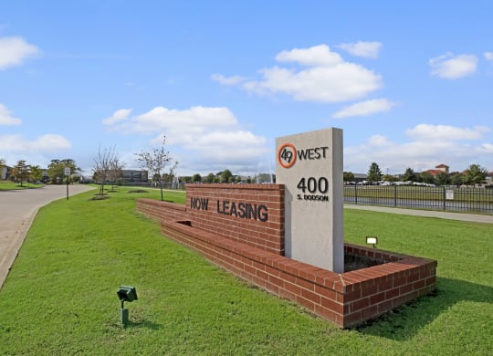 Sign advertising leasing at "49 West, 400 S. Dodson." The sign is on a brick base, surrounded by neatly mowed grass, with a clear sky above.