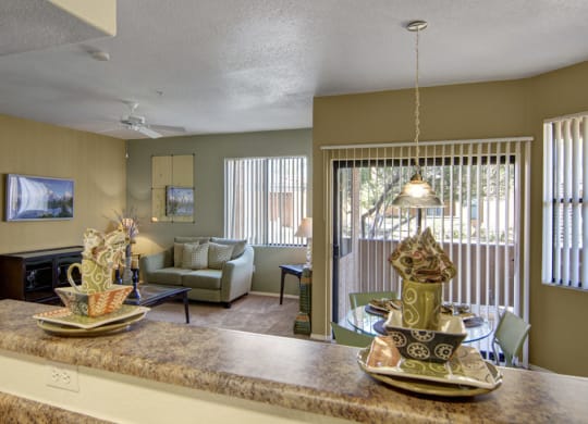 Cozy living area here at Arezzo Apartments with a green couch, round glass dining table, and large windows. Warm tones and decorative dishware create an inviting atmosphere.