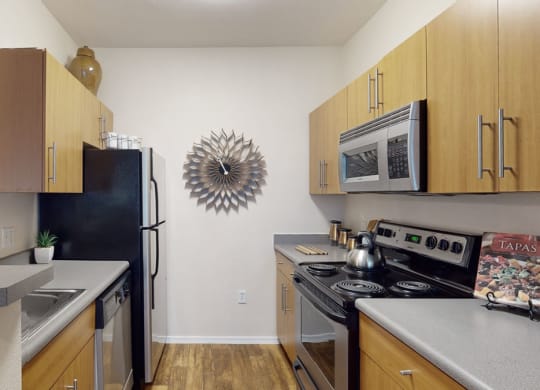 A modern kitchen here at Acclaim Apartments with light wood cabinets, stainless steel appliances, and a decorative metallic wall art. The space feels sleek and organized.