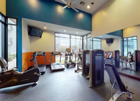 Modern gym here at Acclaim Apartments with exercise machines, including treadmills and weight equipment. Large windows let in natural light, creating an inviting atmosphere.
