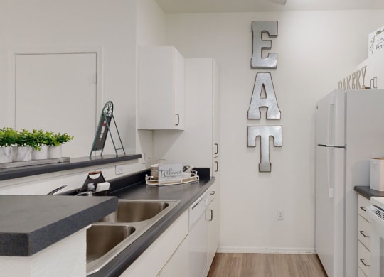 Modern kitchen here at Bolero Apartments with white cabinets, black countertops, and stainless steel appliances. Large "EAT" sign on the wall adds a welcoming touch.