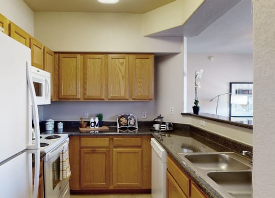 Bright kitchen here at Dobson Towne Centre Apartments with wooden cabinets, granite countertops, and white appliances. A cheerful sign reads "Today is a good day.” Modern and inviting.