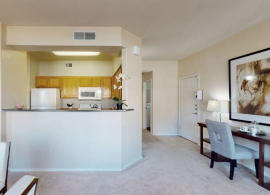 Bright, cozy apartment interior here at Dobson Towne Centre Apartments with an open kitchen featuring wooden cabinets, white appliances, and a small plant. Adjacent dining and living area with soft lighting creates a welcoming ambiance.