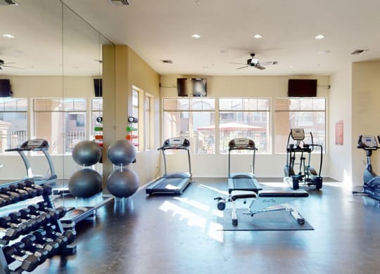 Spacious gym here at Dobson Towne Centre Apartments with treadmills, stationary bikes, free weights, and exercise balls. Sunlight pours through large windows, creating a bright, welcoming atmosphere.