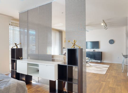 Modern living space here at Rio Paradiso Apartments with a room divider of translucent panels and a black and white shelf. Wooden floors lead to a cozy seating area with a TV console and wall art.