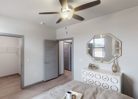 Minimalist bedroom here at 49 West Apartments with light gray walls and doors, a ceiling fan, a dresser with circular patterns, and a geometric mirror. A warm, calm atmosphere.