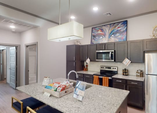 Modern kitchen here at 49 West Apartments with dark cabinets, stainless steel appliances, and a central granite island. A vibrant eye painting adds color above the cabinets.