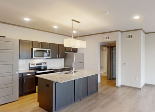 Modern kitchen here at 49 West Apartments view with a granite island, stainless steel appliances, and dark cabinetry. Bright lights create a welcoming, spacious atmosphere.