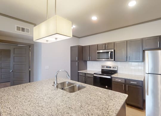 Modern kitchen here at 49 West Apartments with granite countertops, stainless steel appliances, dark wood cabinets, and white tile backsplash. Bright and inviting ambiance.