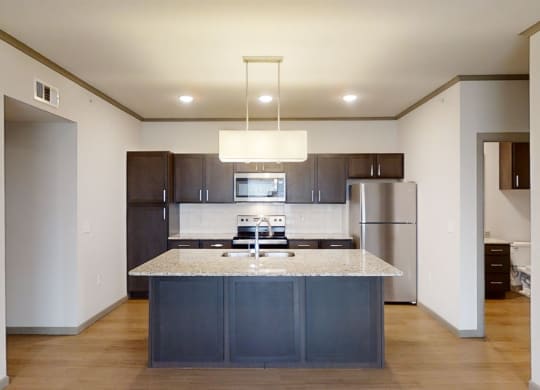 Modern kitchen here at 49 West Apartments with dark wood cabinets, stainless steel appliances, granite island, and pendant lighting. Neutral tones create a sleek, inviting space.