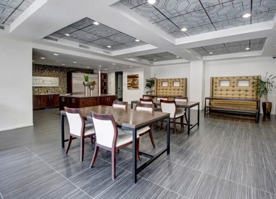 Modern dining area here at Artisan at Main Street Metro Apartments with gray tiled floor, wooden table, and white cushioned chairs. Stylish tufted benches and potted plants add a cozy feel.
