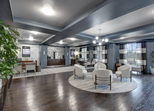 Modern lounge here at Artisan at Main Street Metro Apartments with dark wood floors, round rug, and plush chairs. A coffee station and tables with chairs are along the patterned walls. Bright, airy atmosphere.