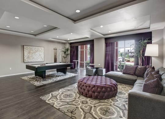 Stylish resident lounge here at Artisan at Main Street Metro Apartments with a pool table on patterned rugs, deep purple curtains, and cozy sofa with matching cushions, creating a luxurious, relaxed ambiance.