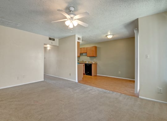 an empty living room with a ceiling fan and a kitchen