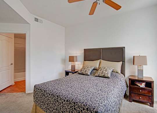 A bedroom with a patterned bedspread and a ceiling fan.
