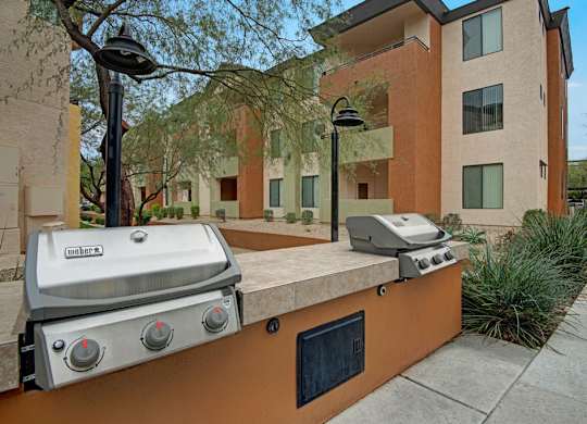 A Weber grill is on a concrete slab outside a building.