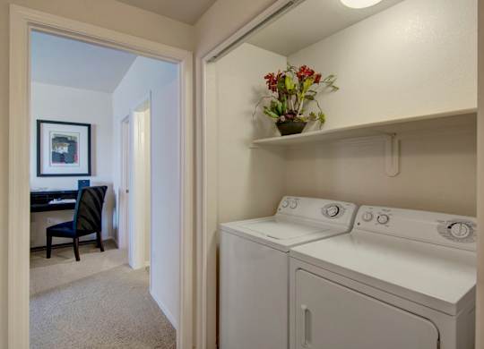 A convenient in-home laundry area here at Bela Rosa featuring a full-size washer and dryer tucked neatly behind sliding doors with an overhead storage shelf. Positioned just off the hallway near a flex space or home office, this dedicated laundry nook offers everyday functionality while keeping the main living areas organized and clutter-free.