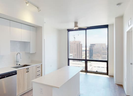A bright and contemporary kitchen here at JOY on 4th featuring sleek white cabinetry, light wood lower cabinets, and polished countertops with a spacious island ideal for dining or entertaining. Stainless steel appliances and a modern tile backsplash complement the clean design, while expansive floor-to-ceiling windows frame stunning city views and fill the space with natural light.
