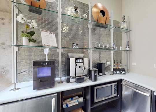 A modern kitchenette with stainless steel appliances and glass shelves.