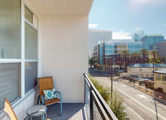 A balcony with a chair and a cushion overlooking a city street.