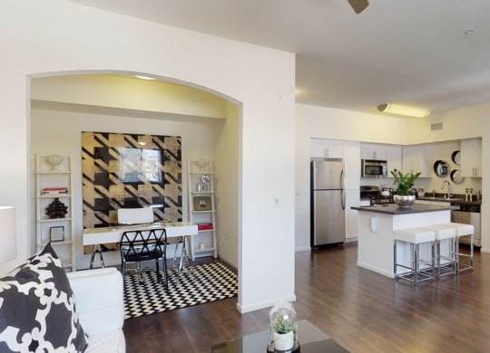 Modern open-plan living space here at Artisan at Main Street Metro with a kitchen, dining, and office area. Neutral tones, sleek furniture, vibrant decor, and natural light create a cozy atmosphere.