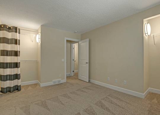 A spacious bedroom here at 3600 Brentwood with soft neutral carpet, warm wall lighting, and convenient open closet storage, creating a clean and comfortable layout.