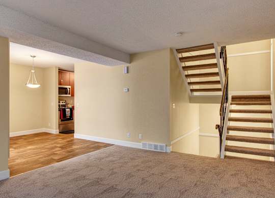 A spacious, open-concept living area here at 3600 Brentwood with soft carpet, warm wood-style flooring in the dining space, and a staircase leading to the upper level, with the kitchen visible just beyond.