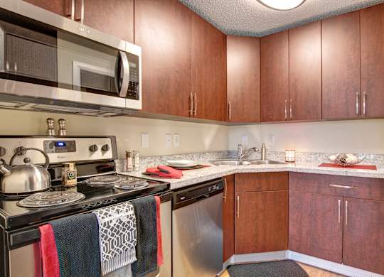 A stylish kitchen here at 3600 Brentwood with rich wood cabinets, speckled granite-style countertops, and stainless steel appliances including a microwave, dishwasher, and stove for a modern, functional space.