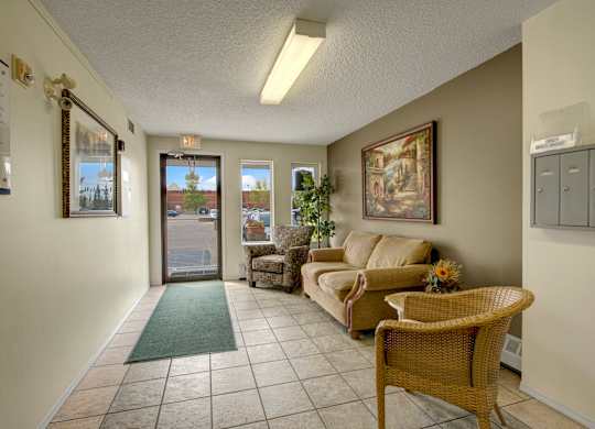 A welcoming lobby here at Aspen Terrace with tiled floors, a cozy seating area, and natural light from large front windows. A comfortable sofa, accent chairs, and warm wall art create an inviting first impression.