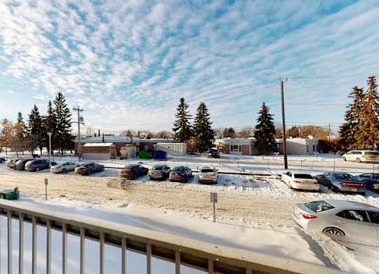 A scenic balcony view here at Cambridge West overlooking a convenient parking area, with tall evergreen trees, open winter skies, and a bright, peaceful neighborhood setting.